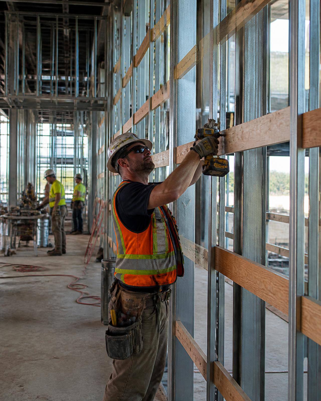 Commercial carpenter fastening wood blocking to metal stud framing on a job site